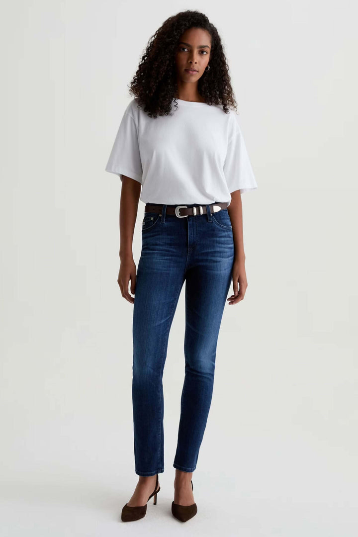 Jean ajusté à taille mi-haute porté avec un t-shirt blanc et talons, coupe ajustée et denim extensible, look décontracté-chic.