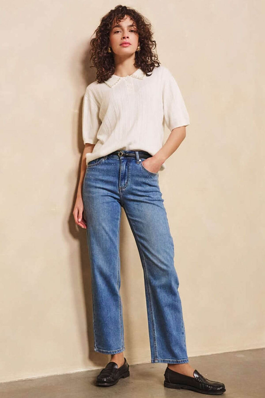 Femme portant un jean droit classique, blouse fluide beige, et chaussures noires sur fond neutre.