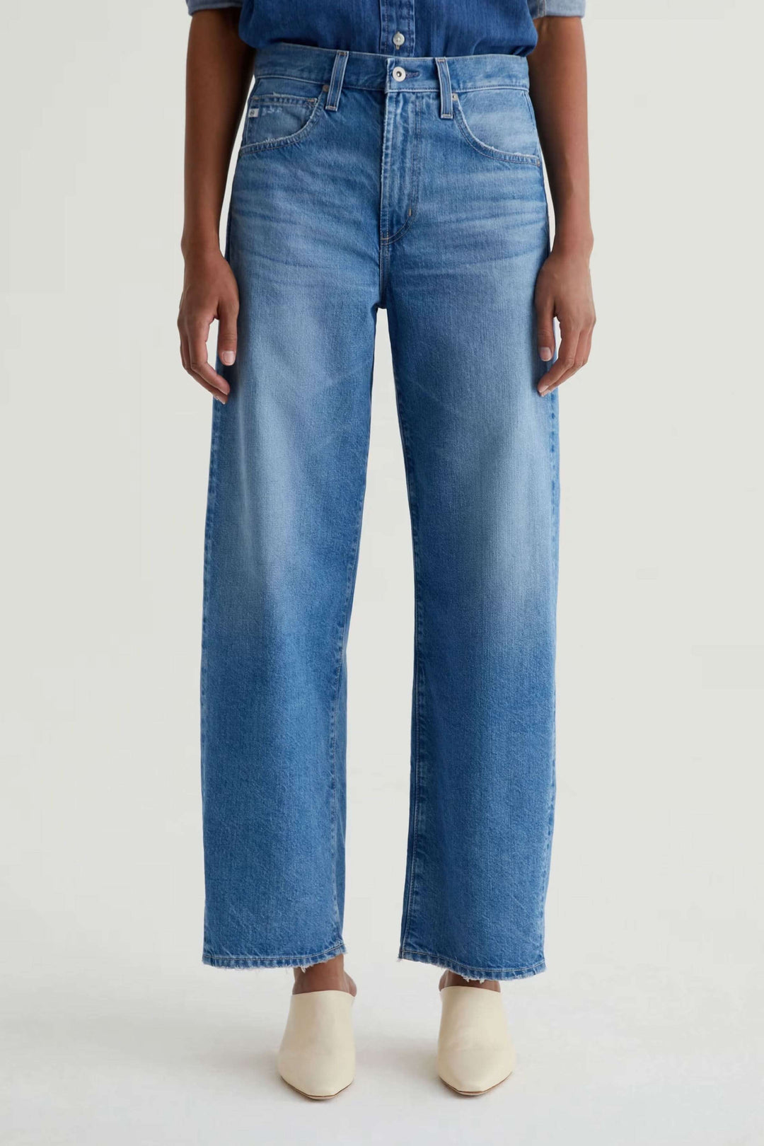 Jean droit à jambe large en denim bleu avec taille haute, présenté avec chaussures blanches et chemise en jean. Confort et allure moderne.