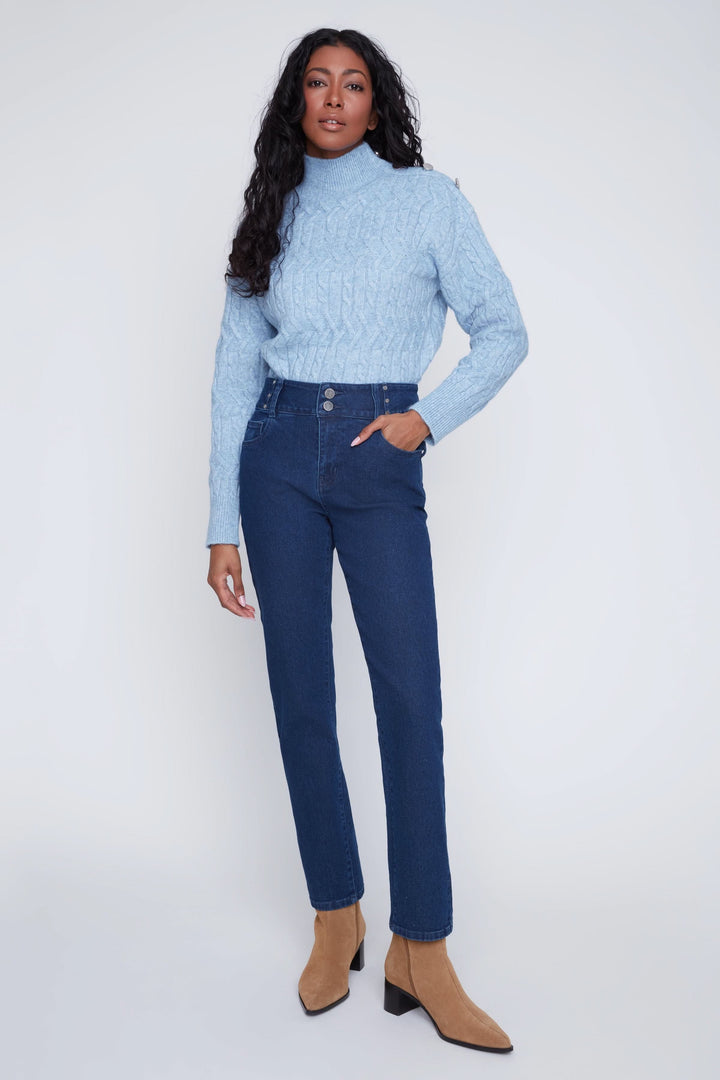 Jean taille haute bleu avec boutons apparents, porté par un mannequin, stylisé avec chandail bleu clair et bottines marron.