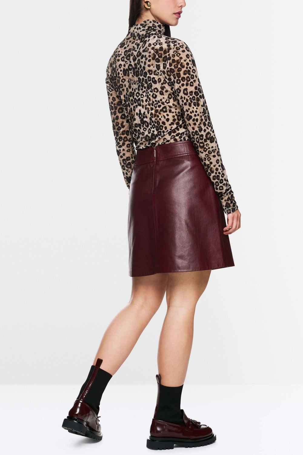 Jupe en cuir bordeaux trapèze, longueur au-dessus du genou, avec une chemise à motifs et des bottines, vue de dos, style moderne.