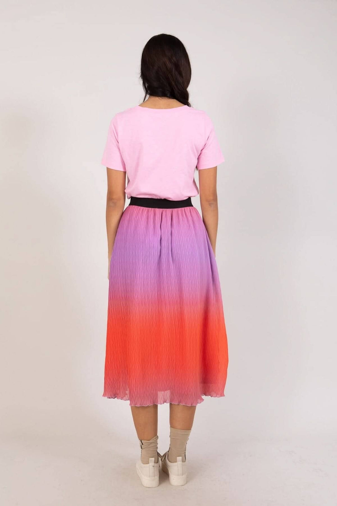 Jupe plissée dégradée en violet et rouge, portée avec un t-shirt rose et une ceinture noire.