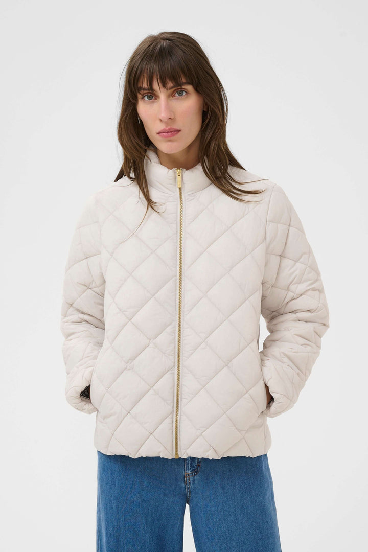 Femme portant un Manteau Olia matelassé blanc, coupe droite, col montant, idéal pour des journées fraîches et un look moderne et pratique.