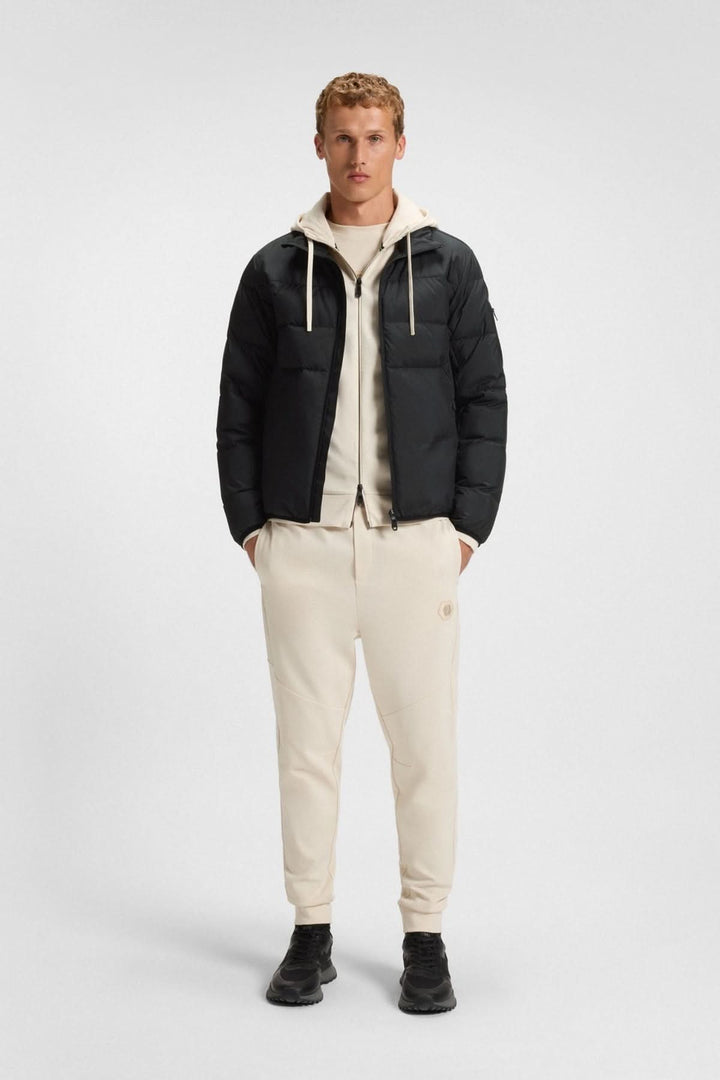 Homme portant un manteau matelassé déperlant en duvet avec poche sur la manche, idéal pour la mi-saison avec style et confort.