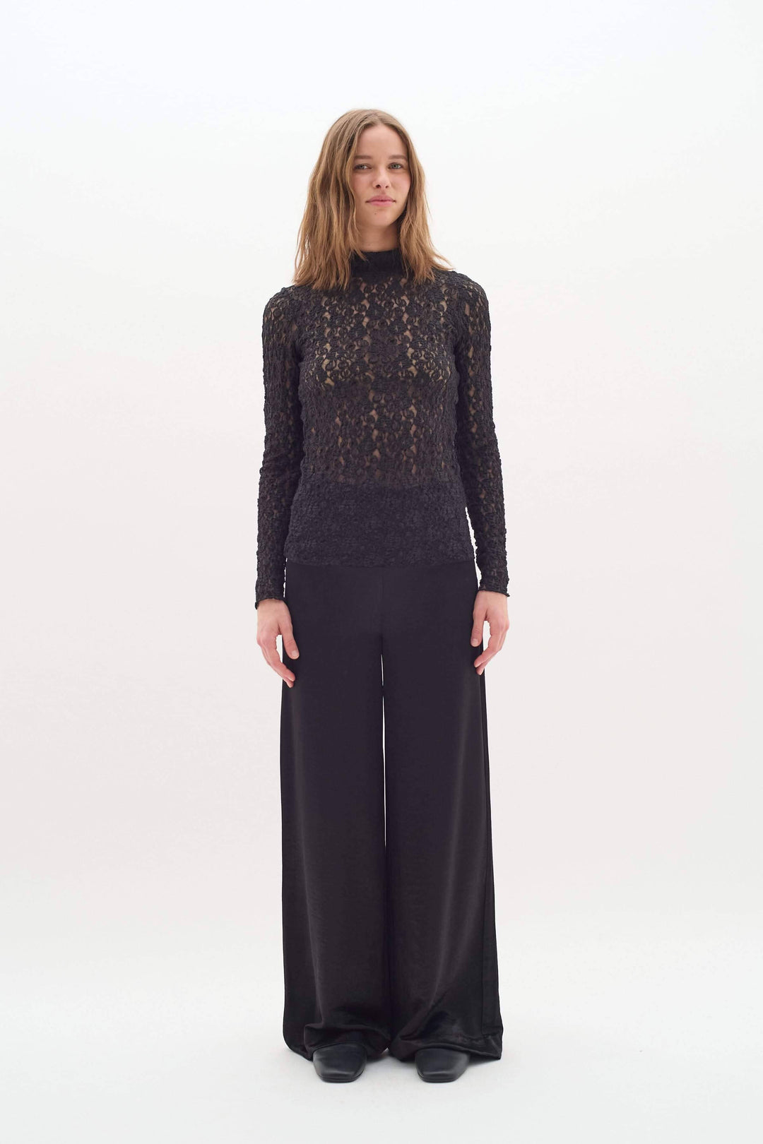 Femme en pantalon Didra noir satiné, look chic et minimaliste, avec top en dentelle. Coupe droite et taille haute pour élégance.
