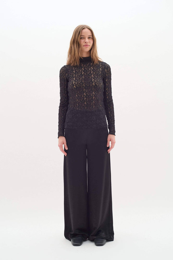 Femme en pantalon Didra noir satiné, look chic et minimaliste, avec top en dentelle. Coupe droite et taille haute pour élégance.