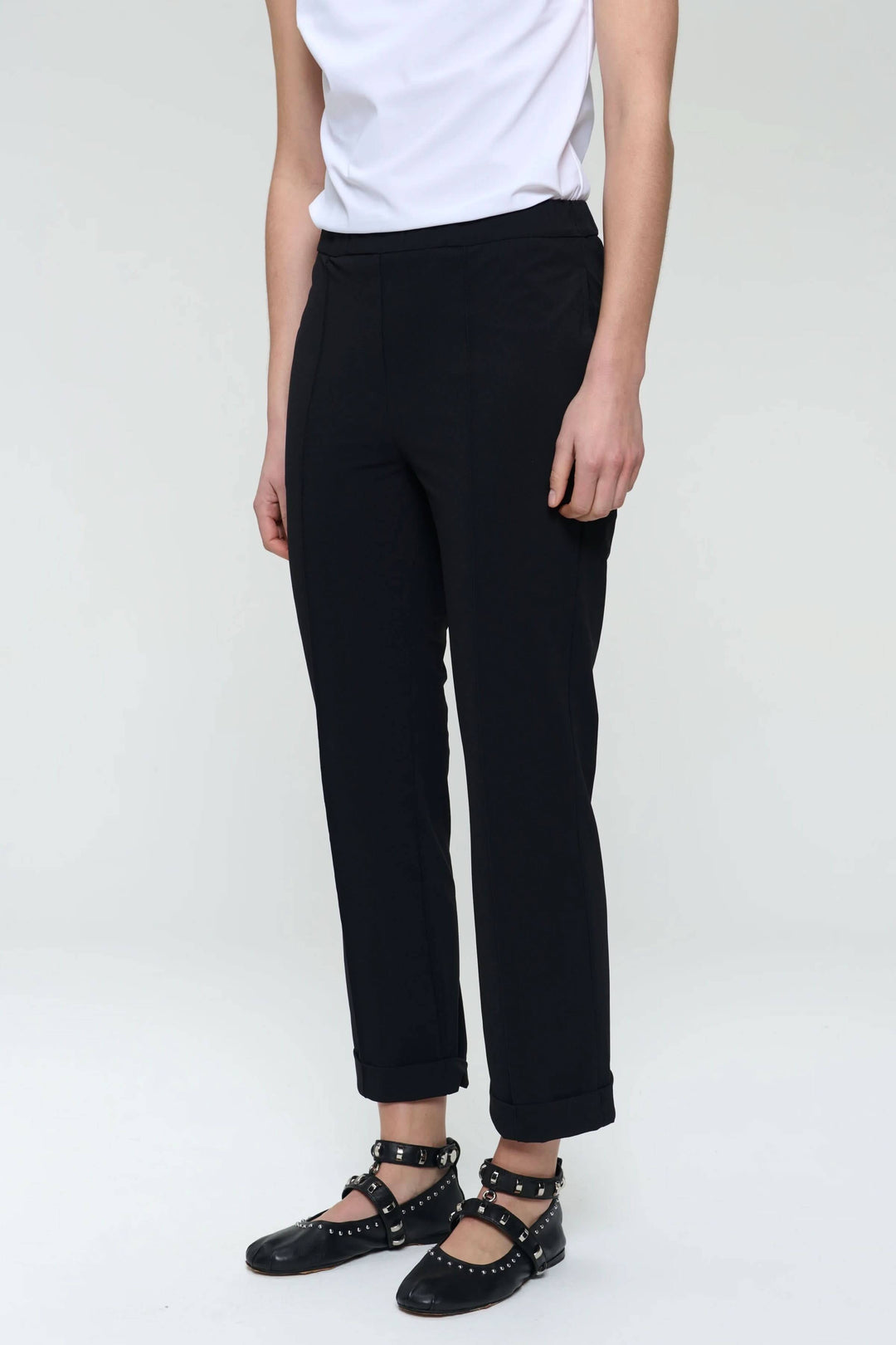 Pantalon Irena noir à revers, coupe droite et tissu extensible, porté avec un haut blanc et chaussures plates.