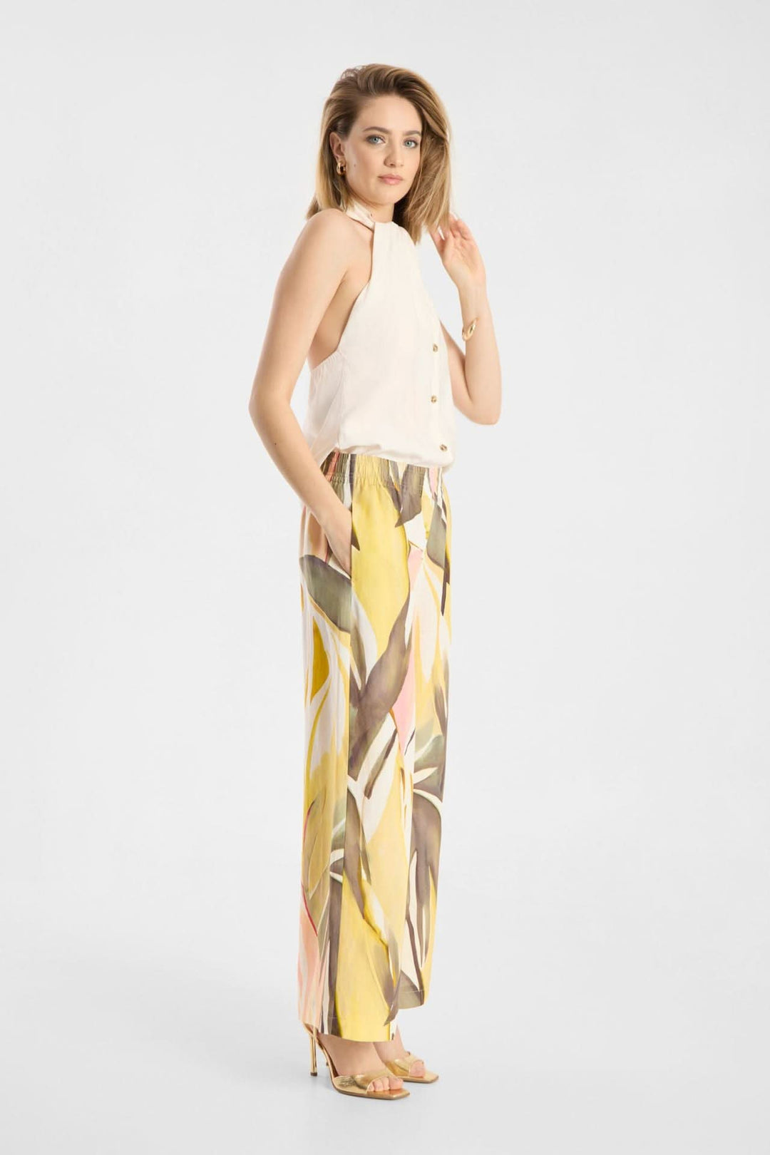 Femme portant un Pantalon Lizett fluide imprimé à taille élastique avec un haut blanc, posant de profil, sur fond blanc élégant.