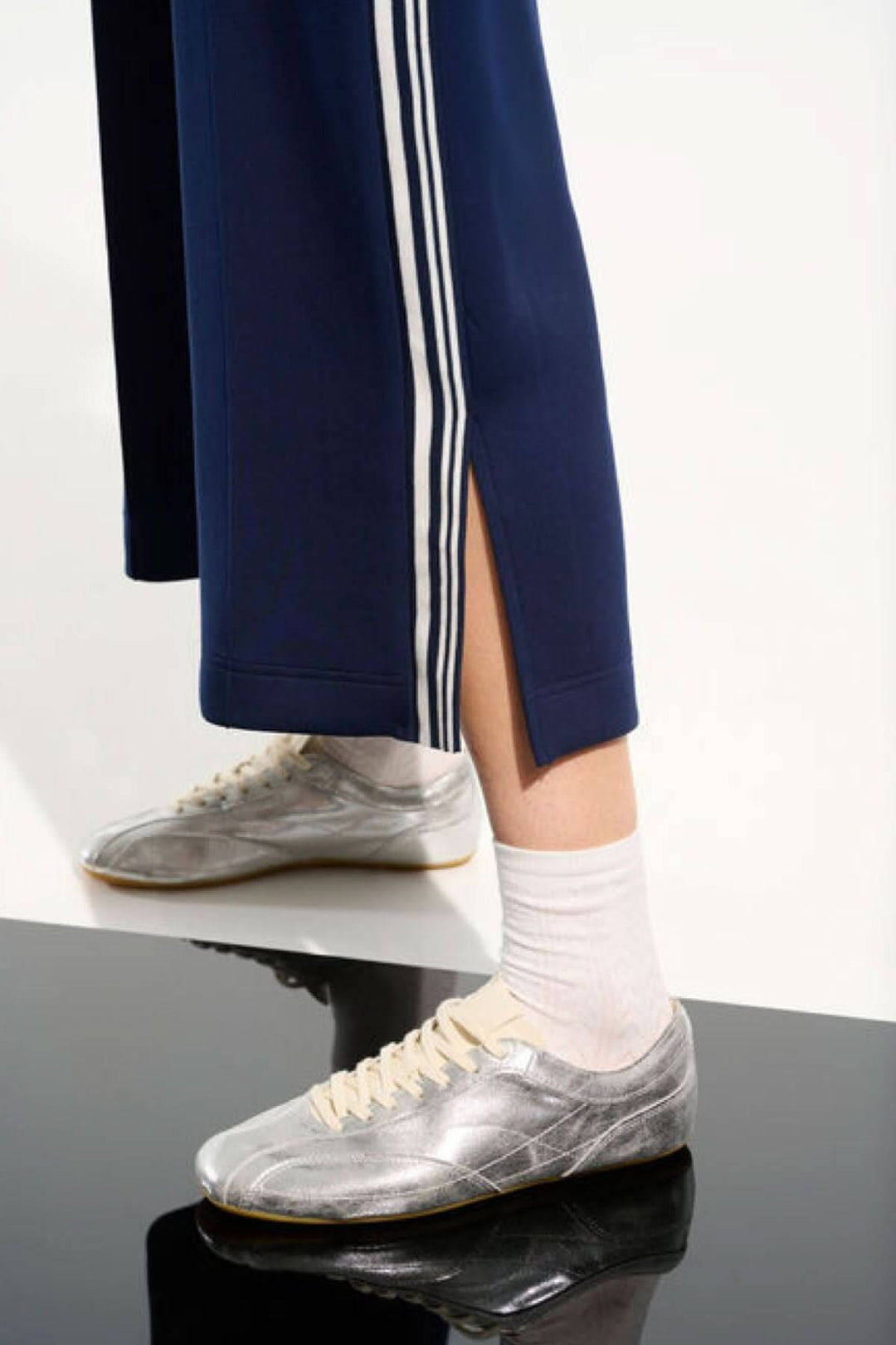 Pantalon athlétique à bandes contrastantes avec fente latérale, style sportif chic, porté avec des baskets argentées.