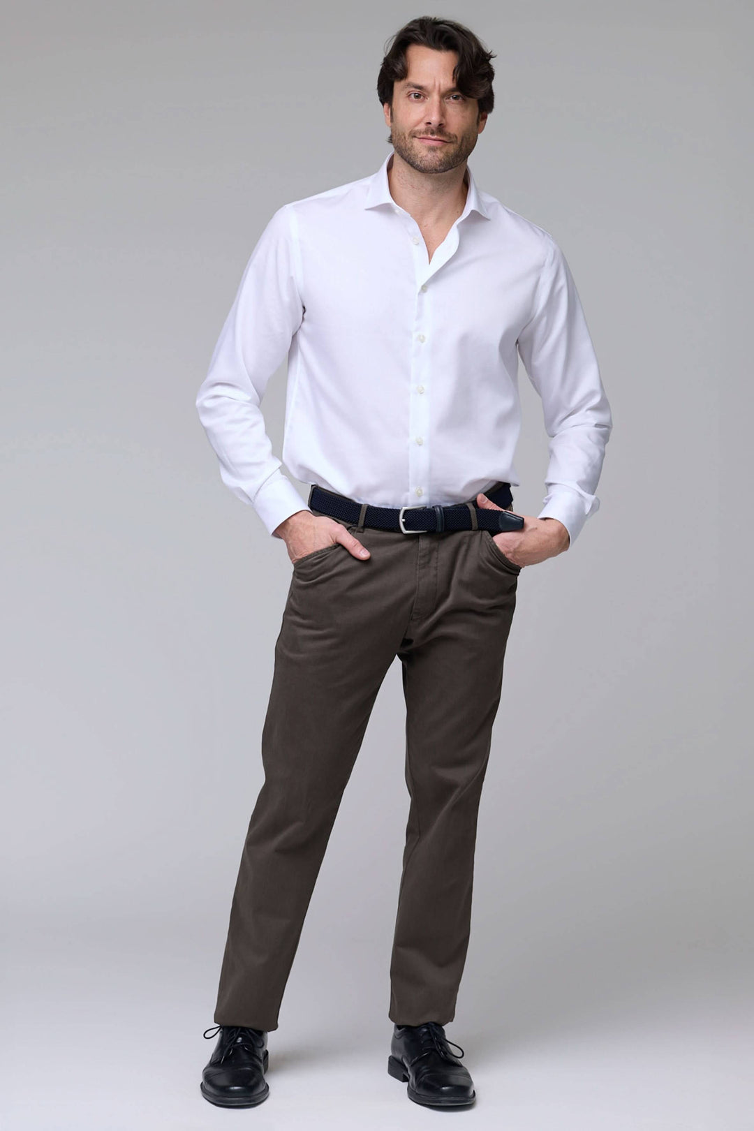 Homme portant un pantalon chino stretch marron avec chemise blanche. Confort et style moderne pour bureau et moments décontractés.