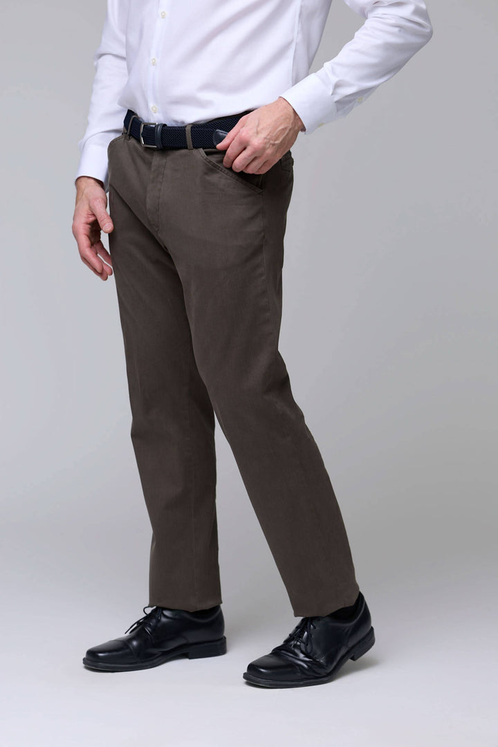 Homme portant un pantalon chino stretch marron avec chemise blanche.