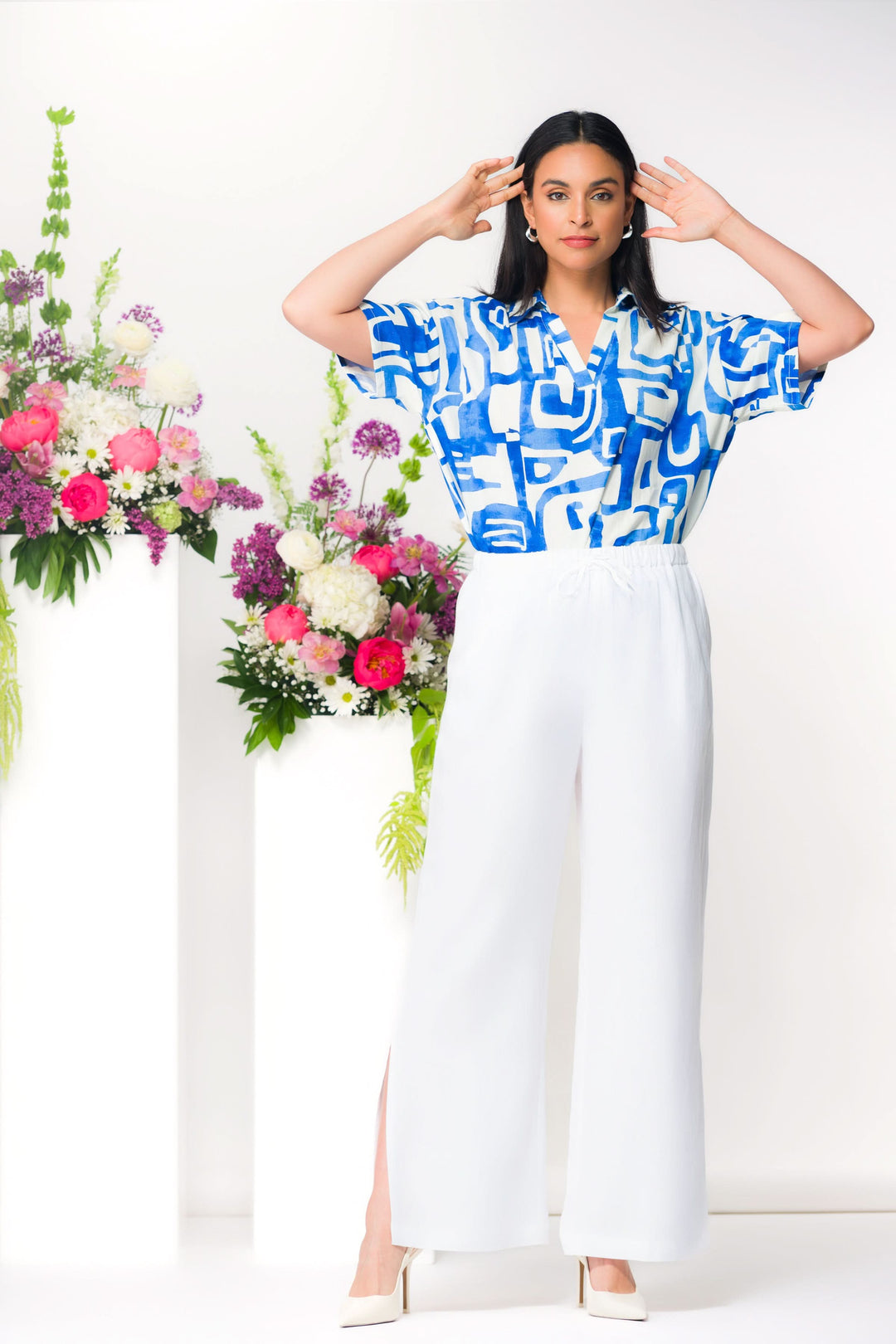 Femme portant un pantalon fluide à fente latérale avec chemise imprimée, devant des fleurs colorées.