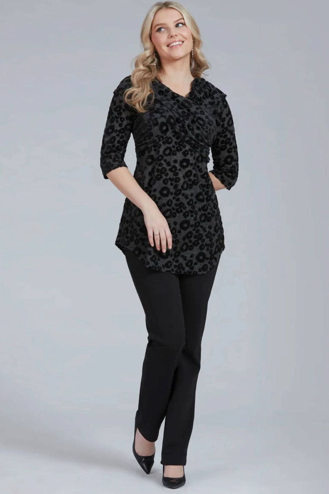 Modèle portant un pantalon habillé Tucker avec blouse noire à motifs, look chic et élégant.