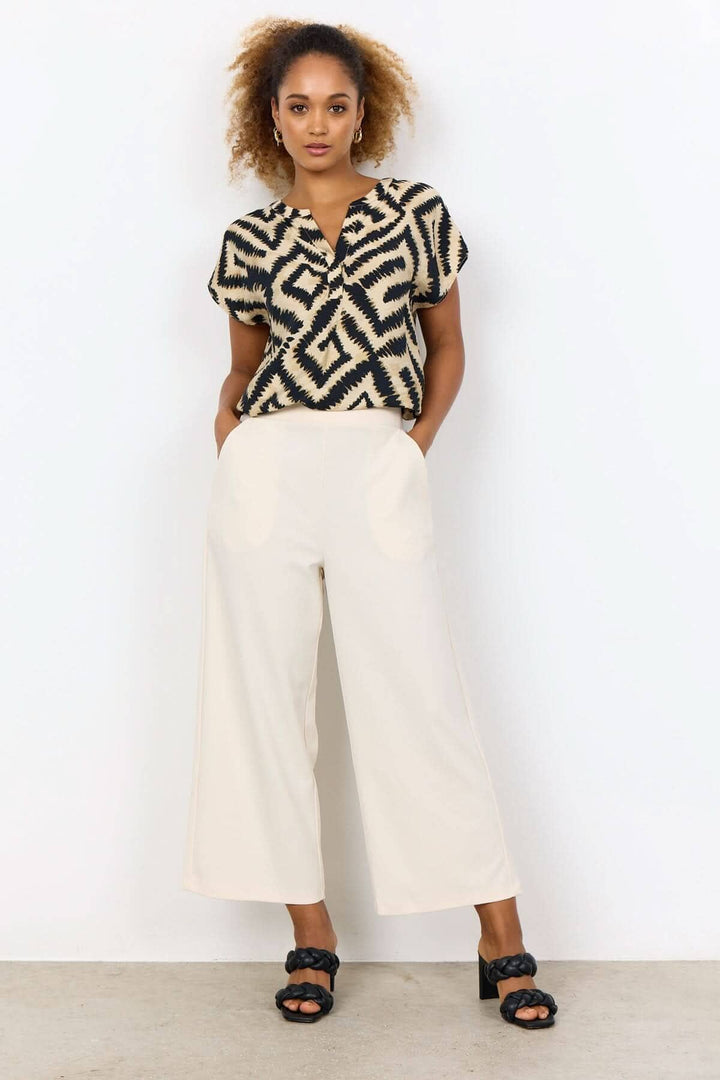 Femme portant un pantalon jambe large beige avec une blouse imprimée, élégante et décontractée.