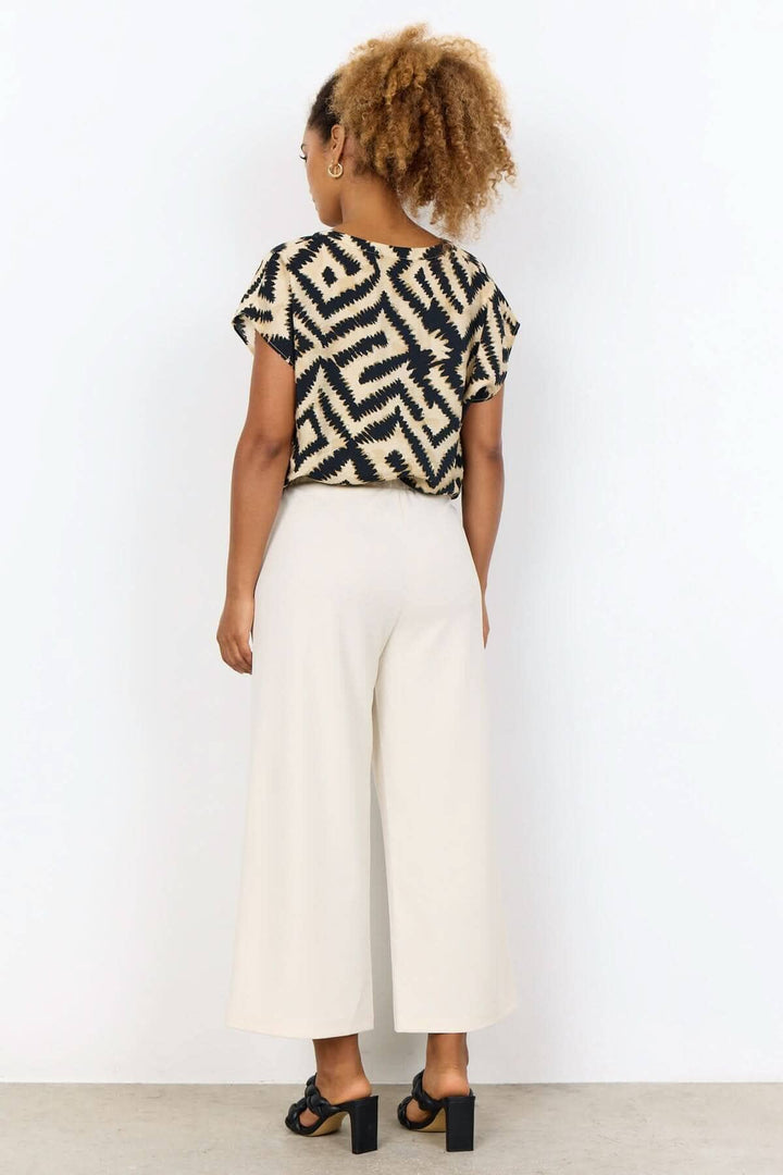 Femme portant un pantalon jambe large beige avec un haut à motif, vue arrière, style décontracté et confortable.