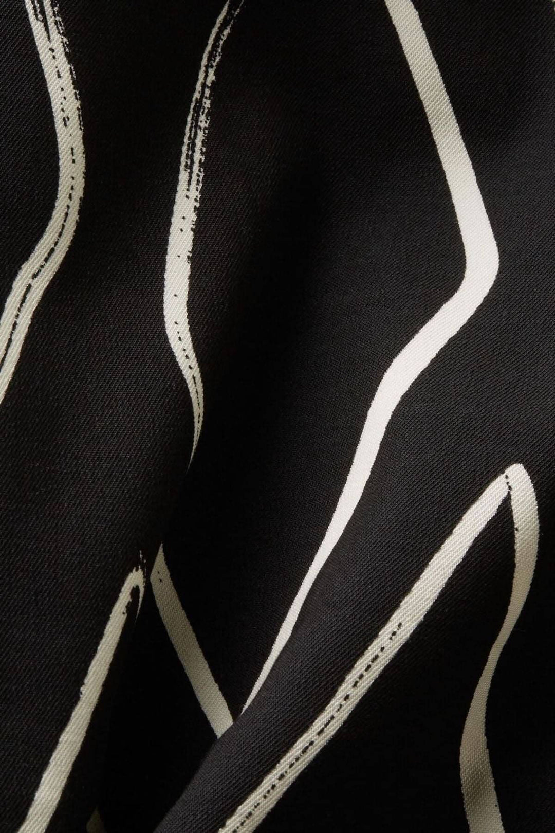Tissu noir avec motifs stylisés en blanc, texture douce et élégante pour un pantalon large imprimé.