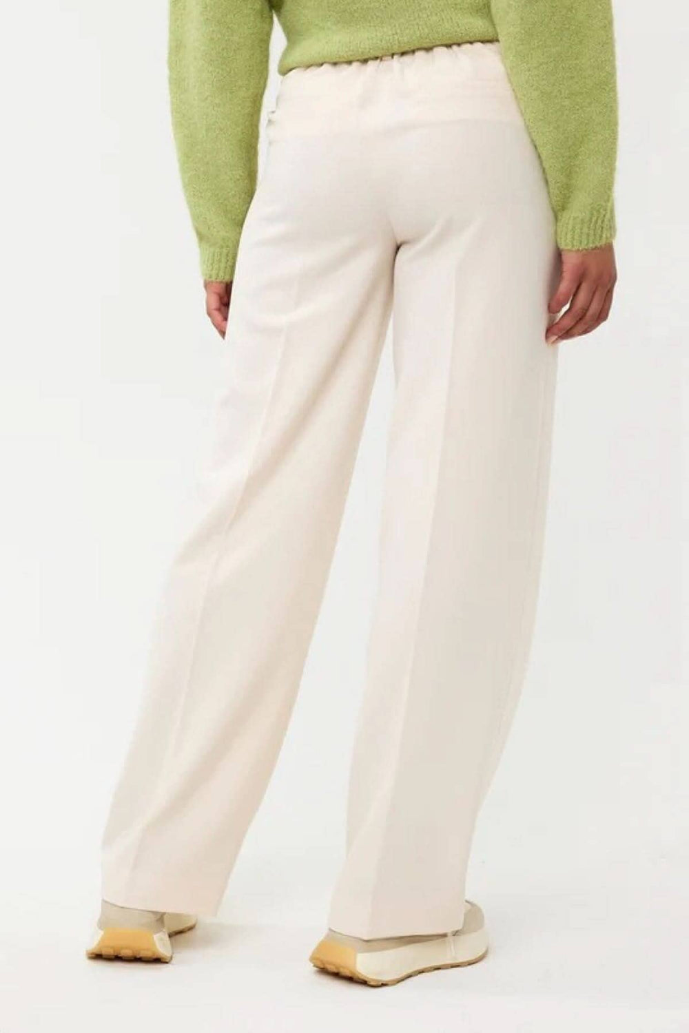 Vue arrière d'un pantalon taille haute à jambe large, beige, avec une taille élastique, porté avec un pull vert.