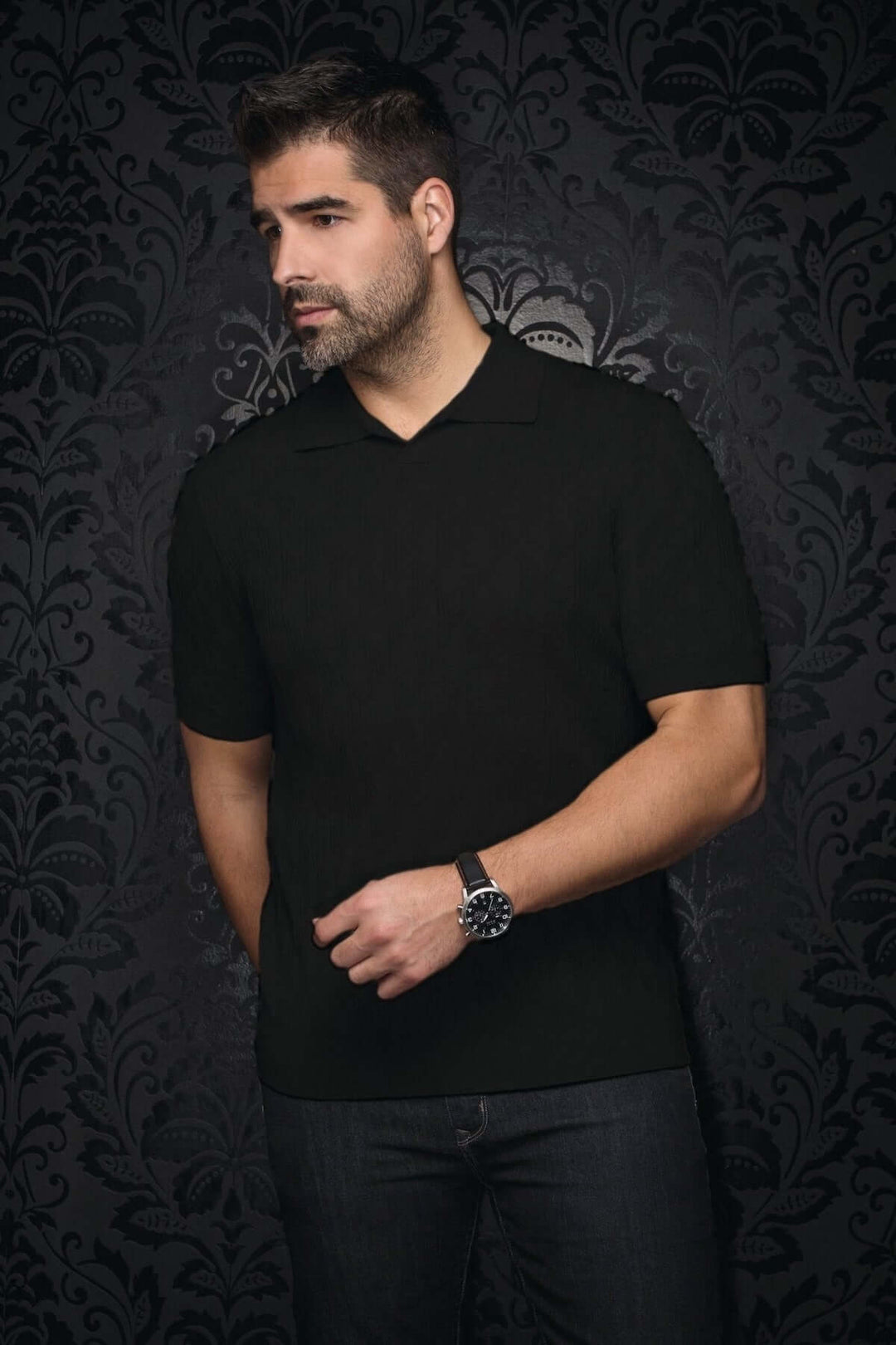 Homme portant un polo noir à col ouvert et manches courtes, avec un fond en damier élégant.