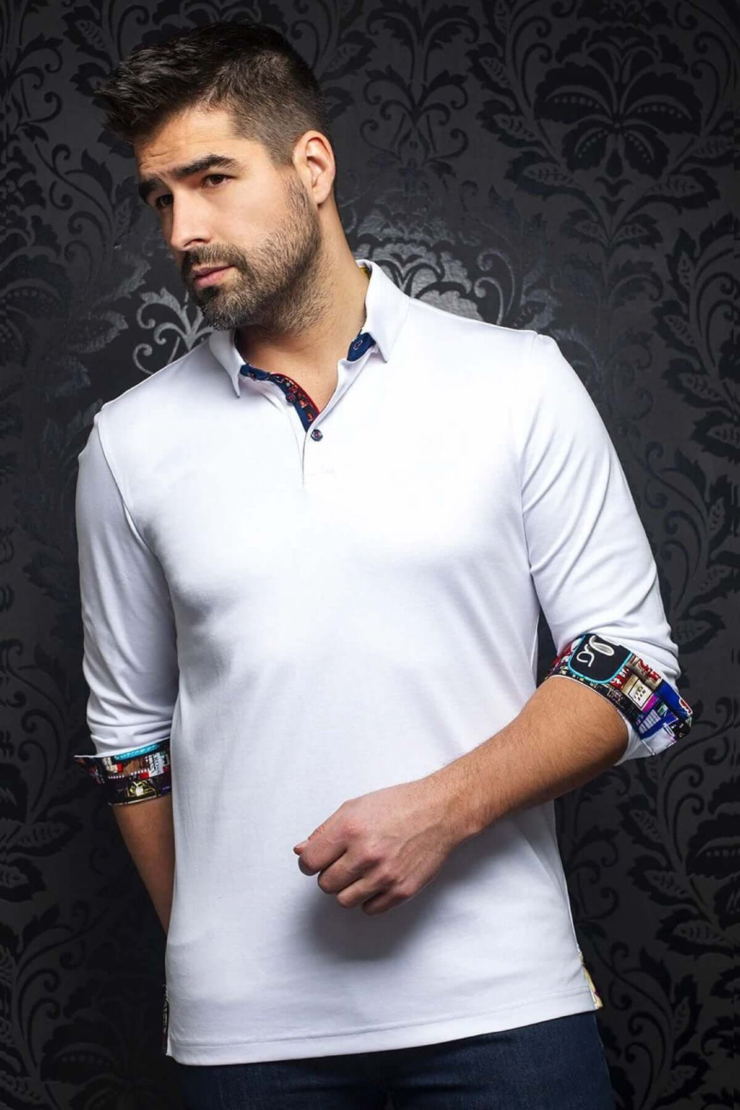 Homme portant un polo blanc à manches longues, avec détails colorés au col et aux poignets, sur fond noir décoratif.