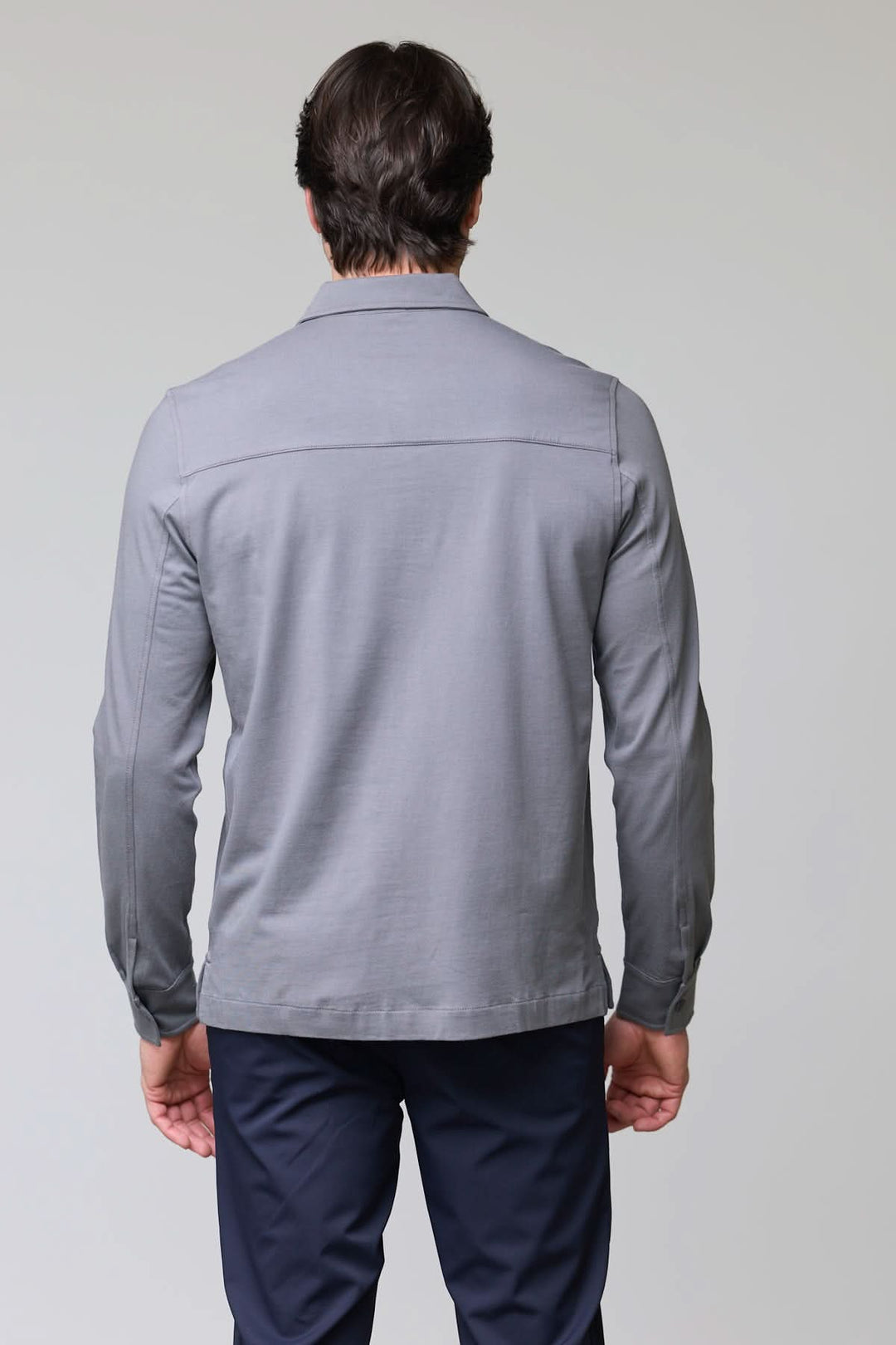 Homme portant un polo à poches boutonnées, manches longues, vue arrière, couleur grise, look décontracté chic.