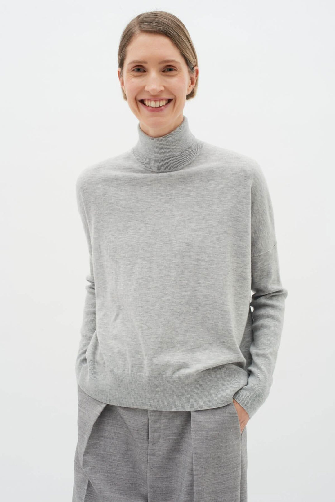 Pull gris à col roulé porté par une femme, alliant confort et élégance, parfait pour une allure sophistiquée.