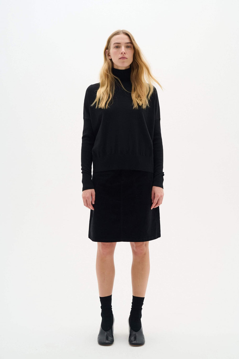 Pull noir à col roulé Kellsie porté avec une jupe, présentant une élégance et un confort optimal.