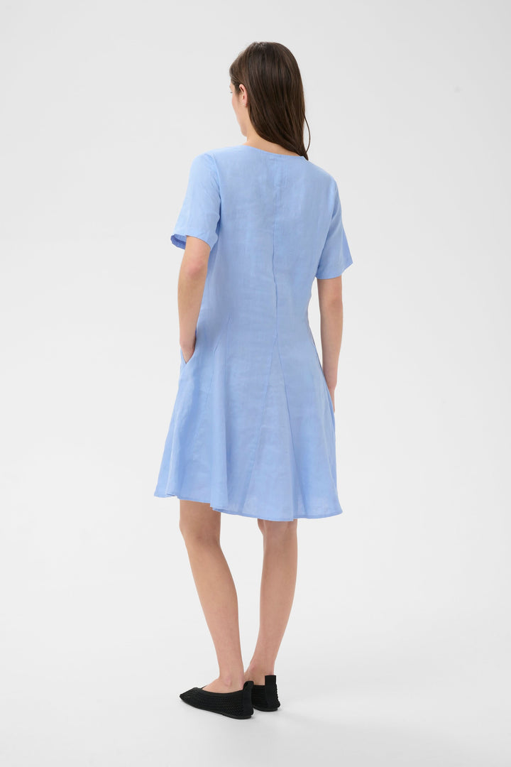 Robe Aminasa bleue, coupe fluide légèrement évasée, encolure en V, manches courtes, poches latérales pour un style élégant et naturel.