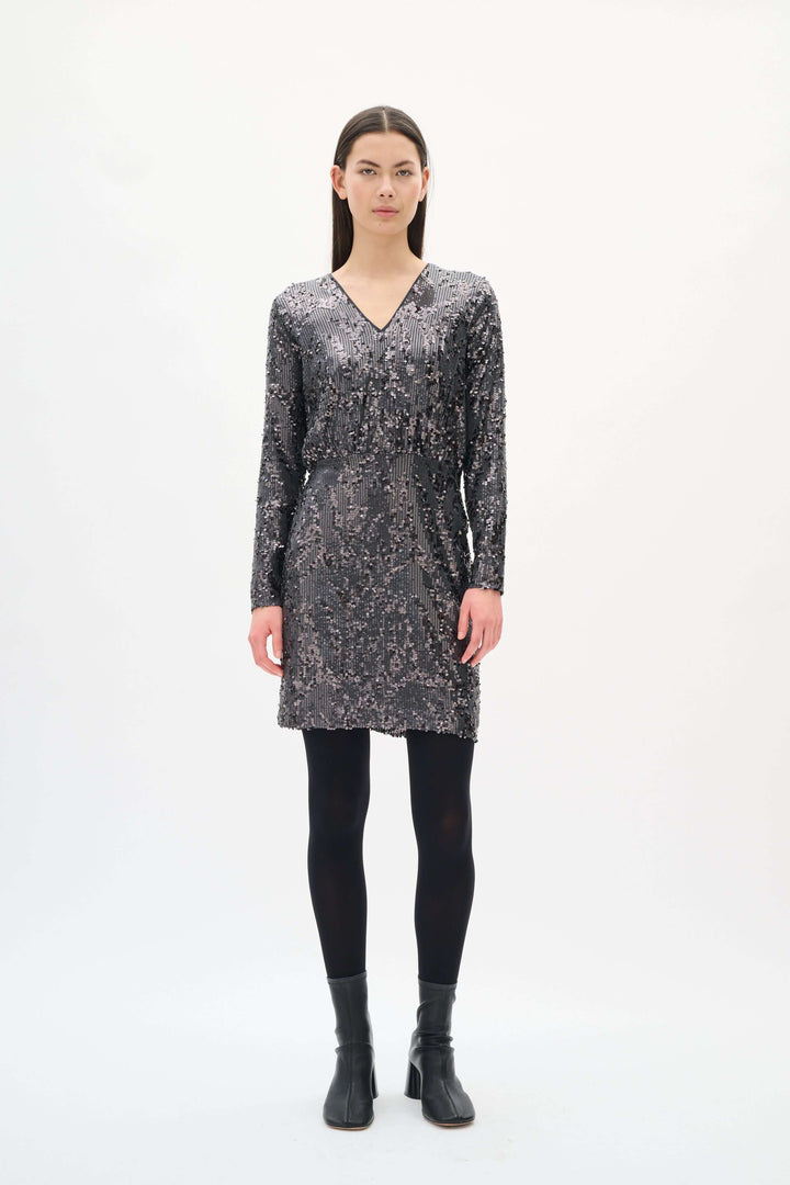 Femme portant la Robe Kimba à paillettes à manches longues avec col en V, coupe élégante pour soirées festives.