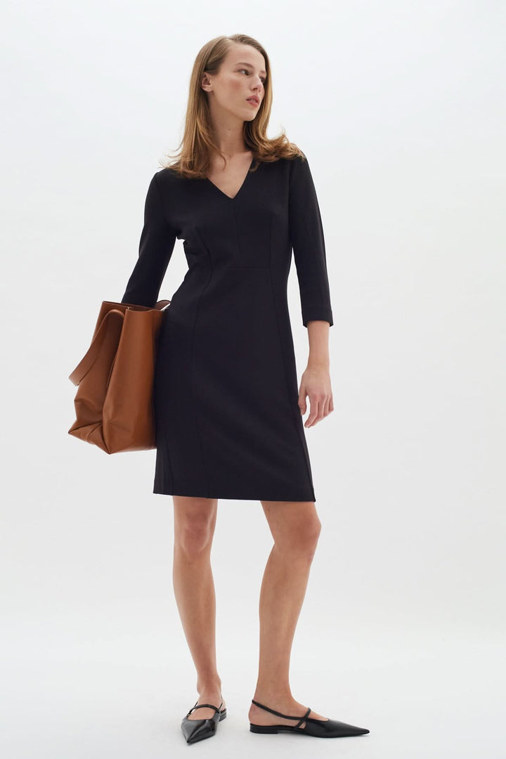 Femme portant une robe droite col V Pannie noire avec manches longues, accessoirisée d&