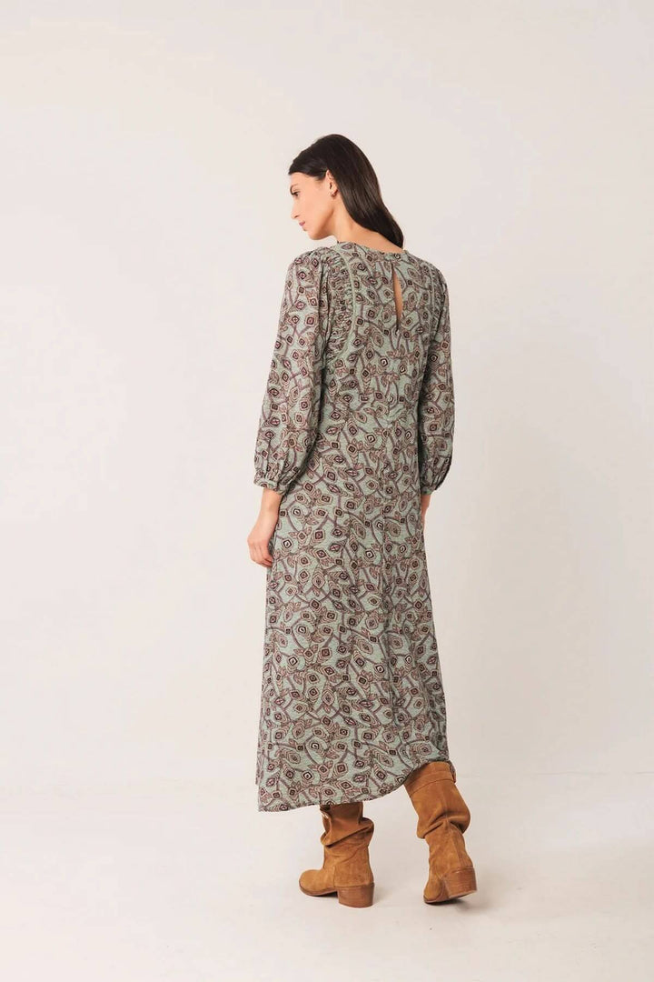 Femme portant une robe longue au motif géométrique avec manches bouffantes et bottes en daim, vue de dos.
