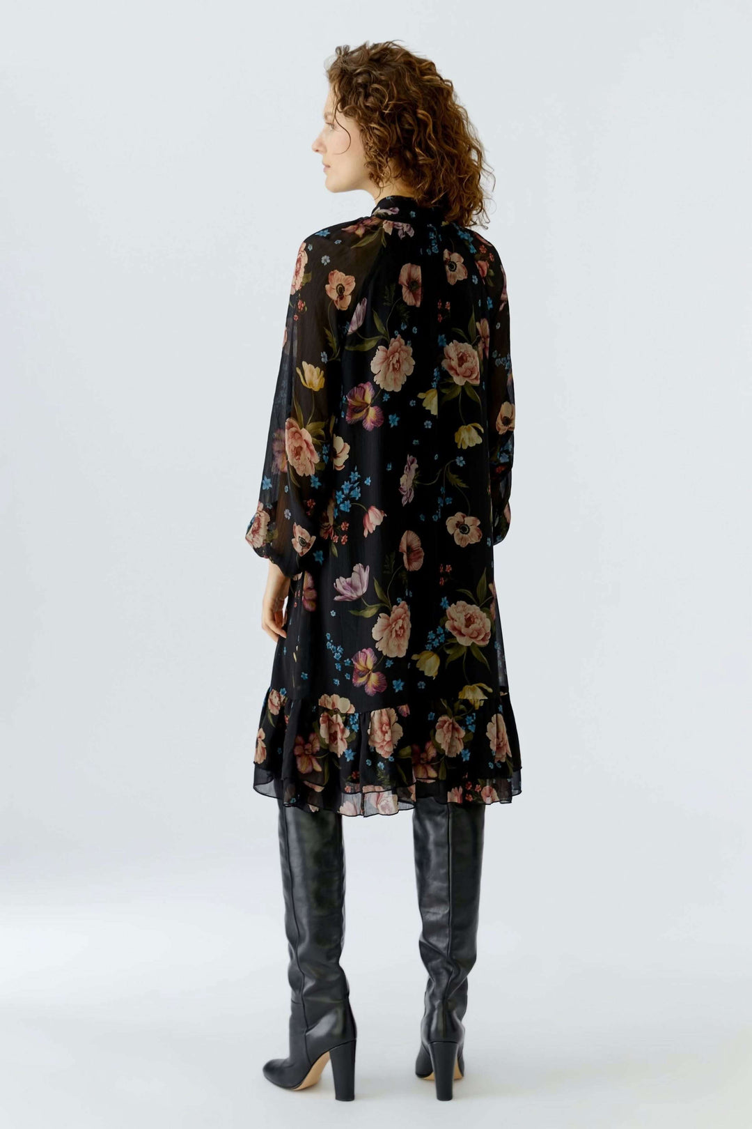 Robe midi fluide à imprimé floral, encolure nouée, portée avec des bottes, vue arrière élégante.