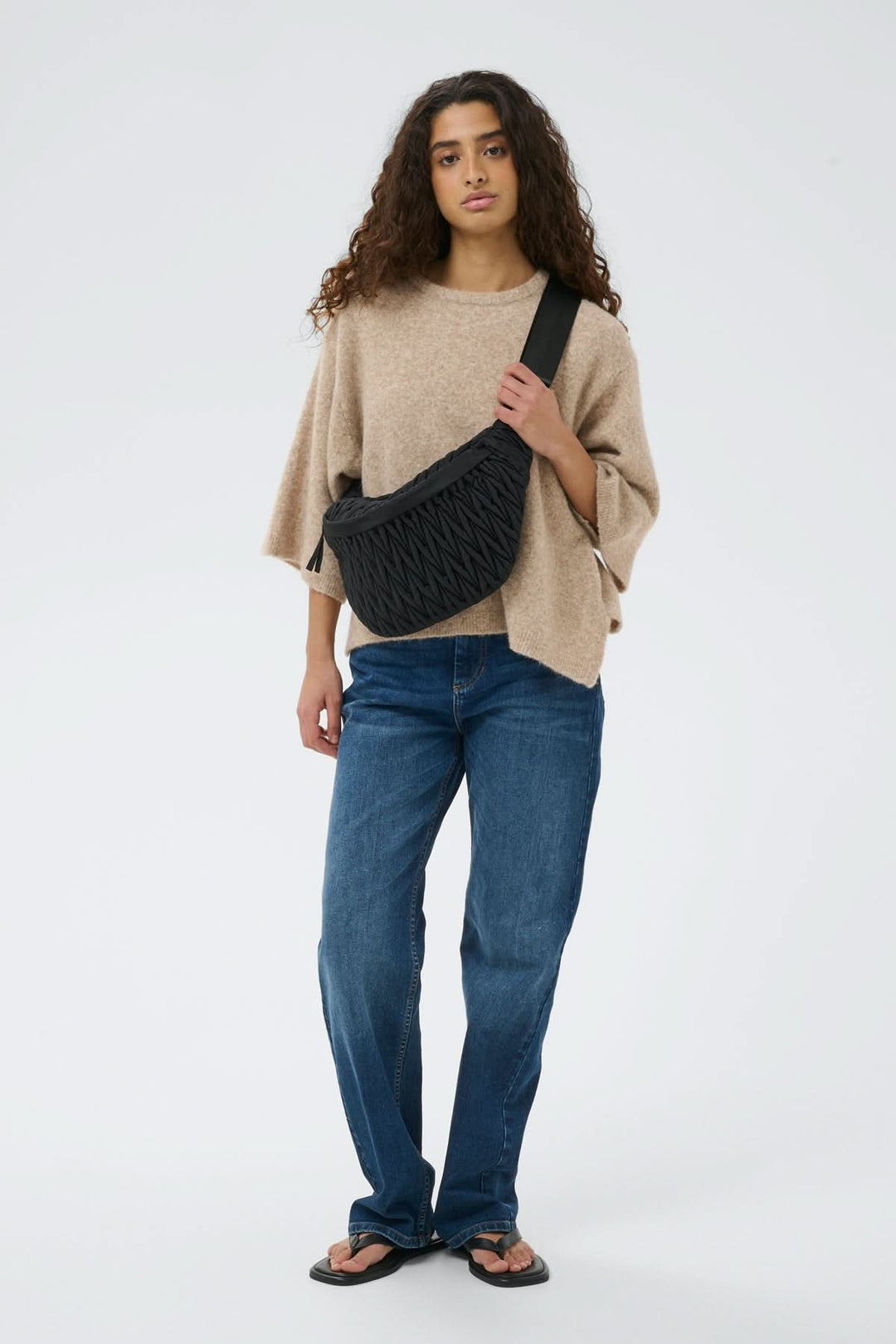 Femme portant un Sac bandoulière matelassé Samy Bumbag noir avec texture froncée, tenue urbaine décontractée.