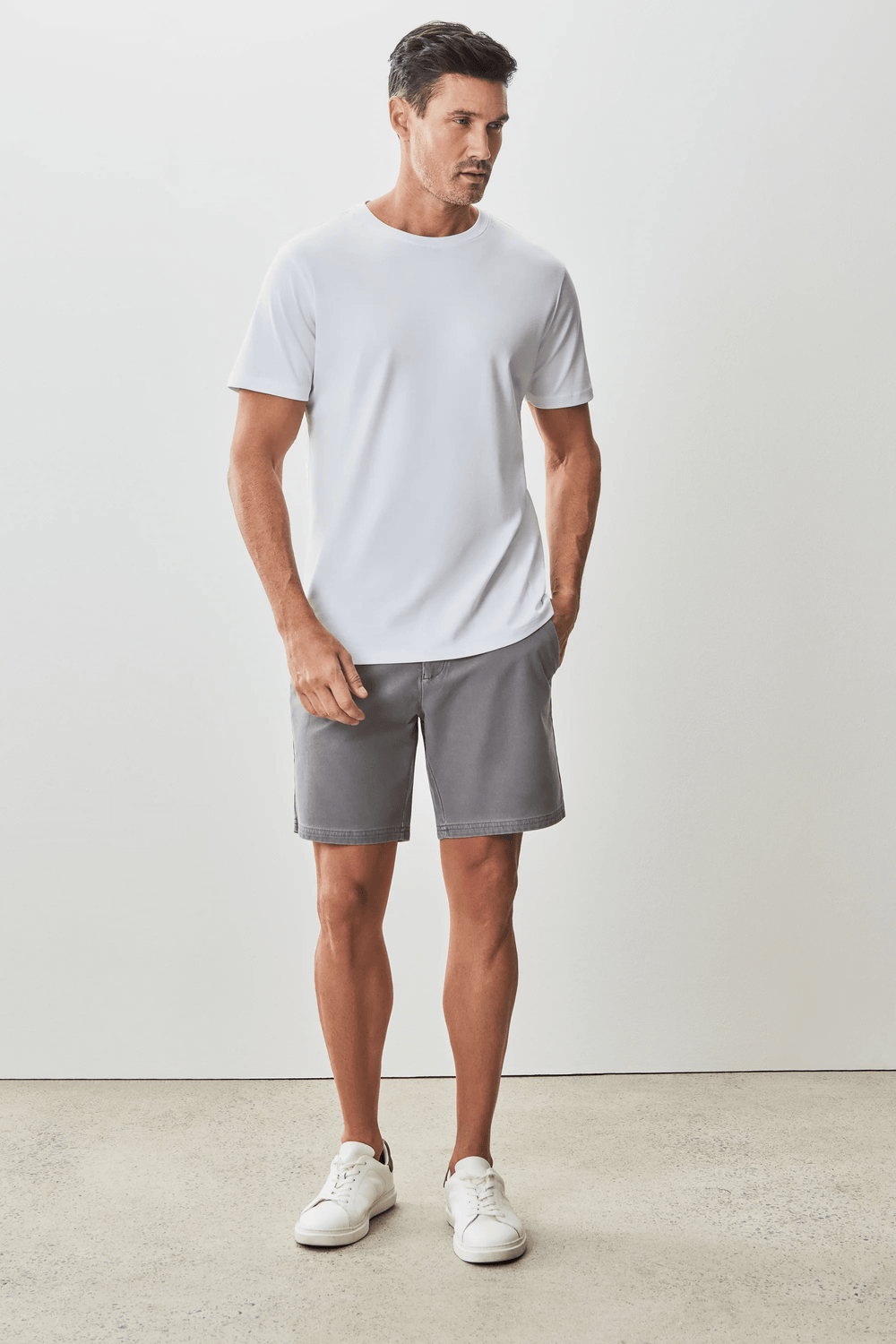 Homme portant un t-shirt blanc moderne et élégant avec un short gris, style minimaliste.