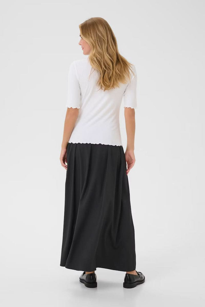 Femme portant le T-shirt Ribba blanc à col montant et manches mi-longues avec une jupe noire, vue de dos.