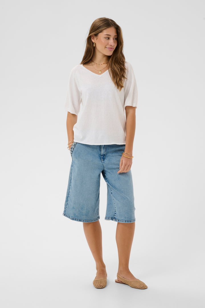 Femme portant un T-shirt Romane blanc avec encolure en V et manches amples, style décontracté.