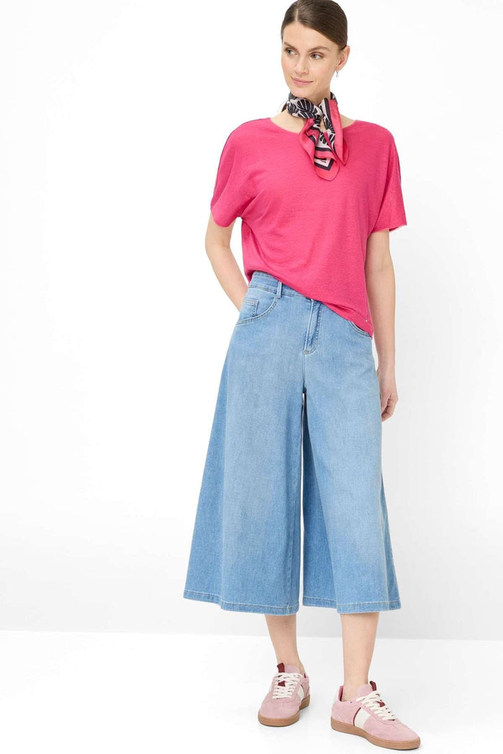 Femme portant un T-shirt col bateau Caelen rose avec un pantalon en denim large, look moderne et décontracté.