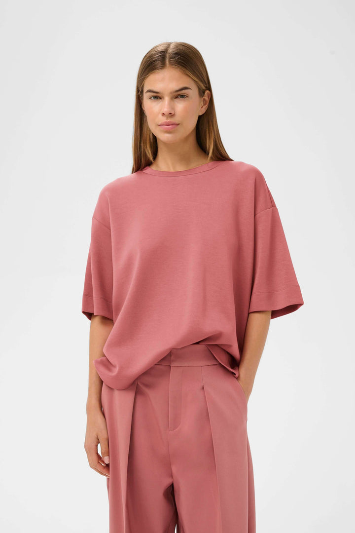 Femme portant un T-shirt coupe ample Pannie rose avec pantalon assorti, style décontracté et moderne.