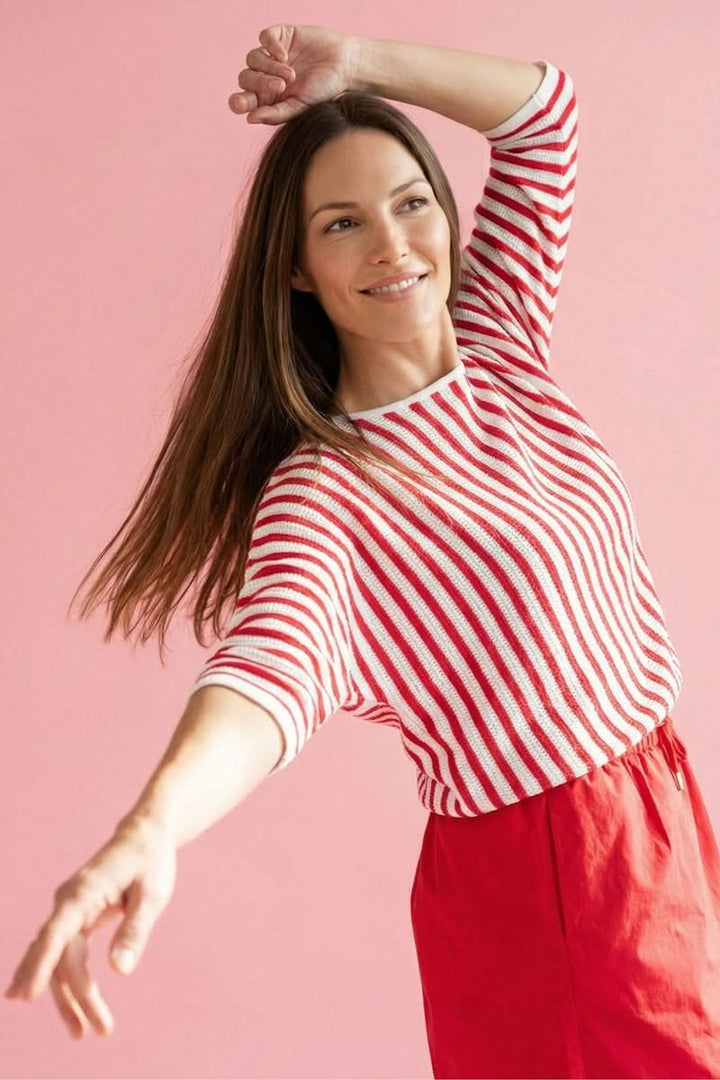Femme portant un tricot rayé manches trois-quarts rouge et blanc, assorti avec une jupe rouge, sur fond rose.