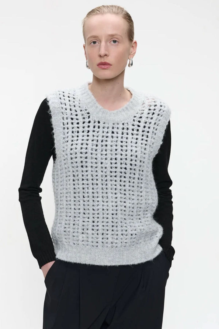 Tricot sans manches en maille ajourée porté sur un haut noir pour un look moderne et chic.