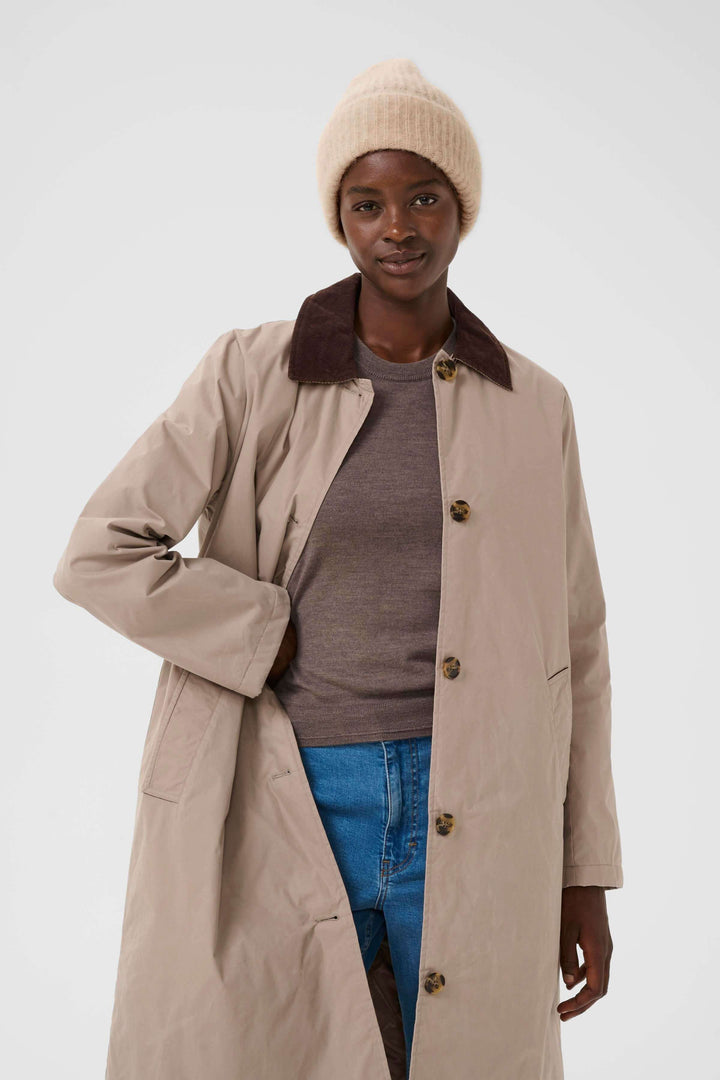 Personne portant une Tuque Sanja en tricot côtelé, avec manteau beige et chemise marron pour un look hivernal moderne.