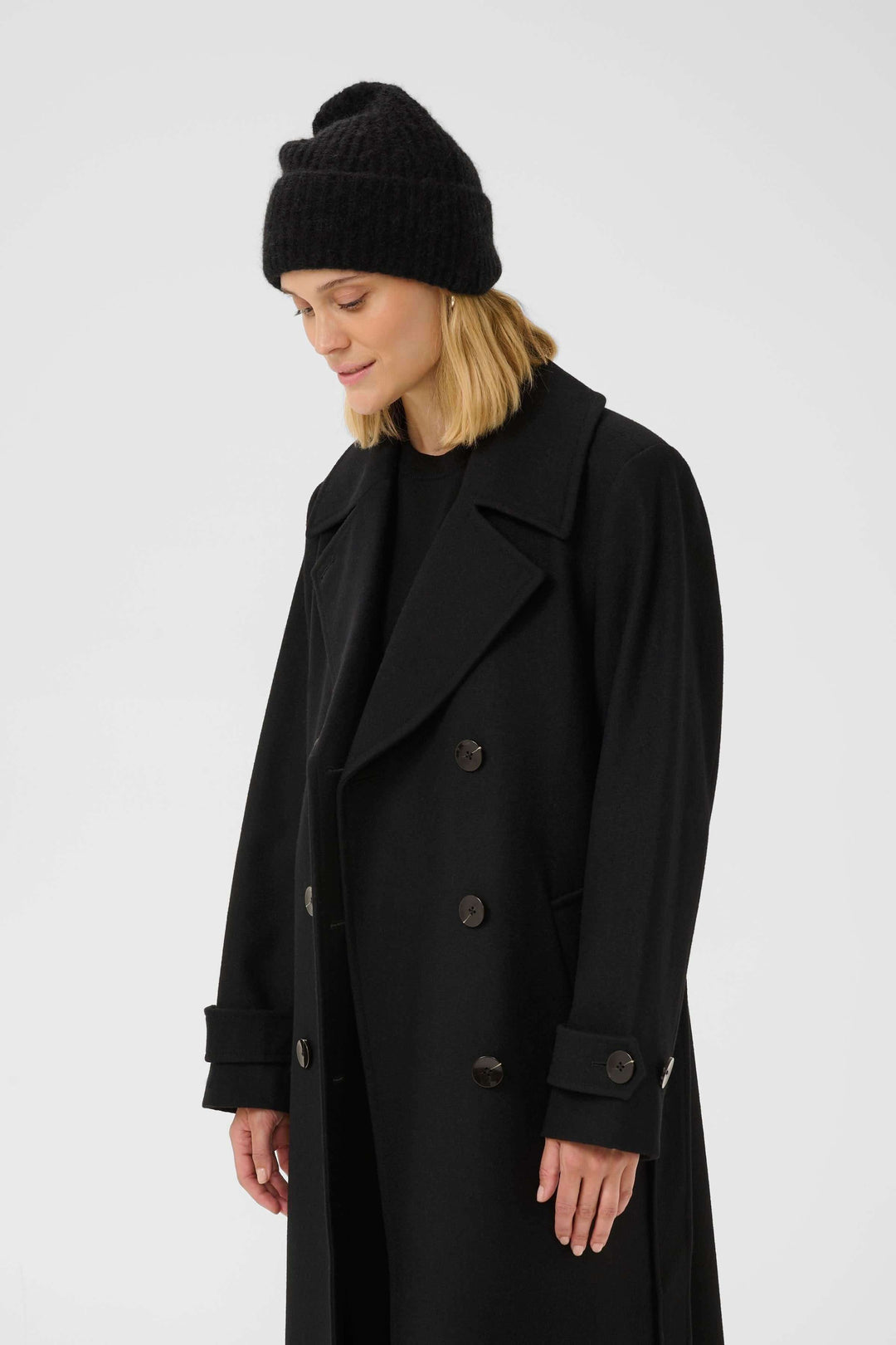 Femme portant un manteau noir et la Tuque Sanja en tricot côtelé, style urbain et moderne.