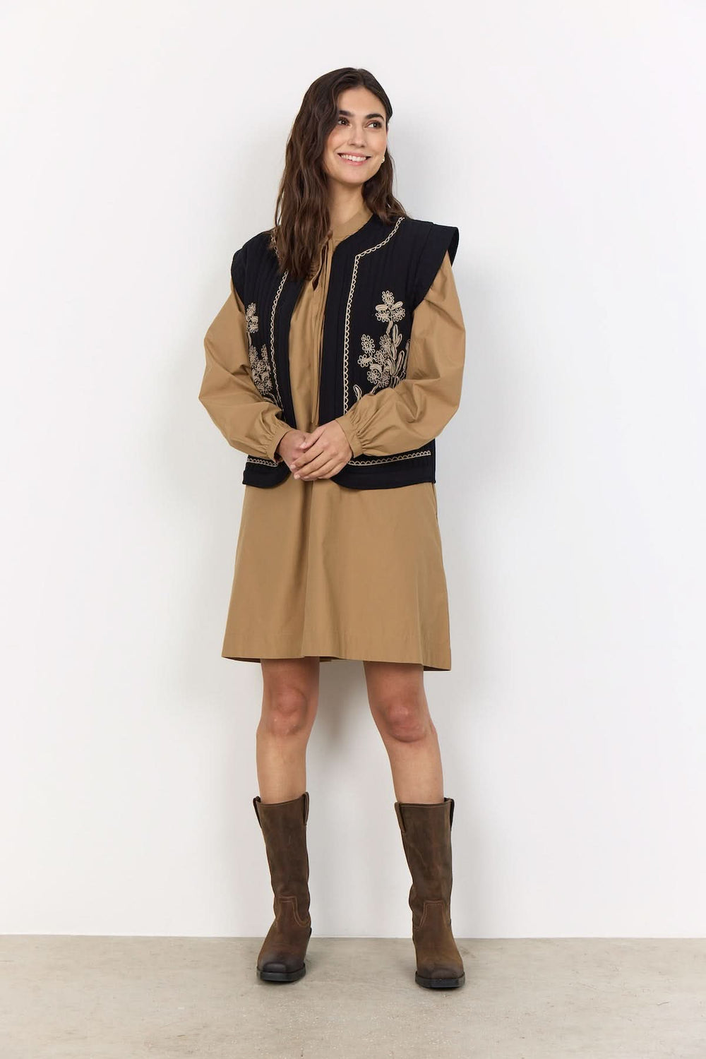 Femme portant une veste courte sans manches avec broderies florales, offrant un style décontracté et féminin.