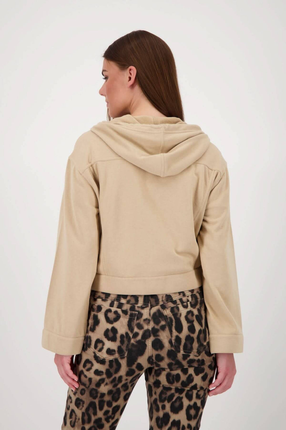 Femme portant une veste courte à capuchon beige avec un pantalon à imprimé léopard, vue de dos.