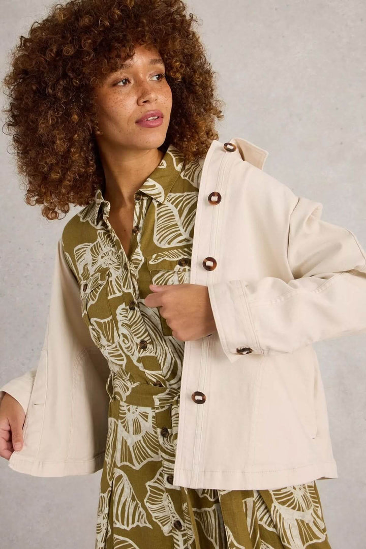Veste en denim Eden à col portée sur une robe imprimée avec un mur gris en arrière-plan.