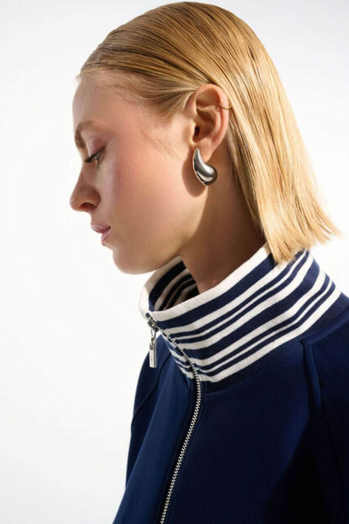 Femme portant une veste zippée à rayures contrastantes avec col rayé, coupe droite et manches trois-quarts, style chic et décontracté.