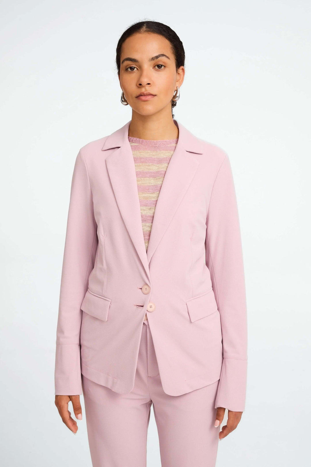 Veston Amsterdam rose structuré avec col tailleur et boutons, porté sur un haut rayé.