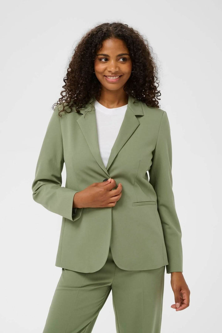 Veston à coupe droite, vert olive, porté par une femme, style élégant et moderne, col tailleur, pour bureau ou occasions habillées.