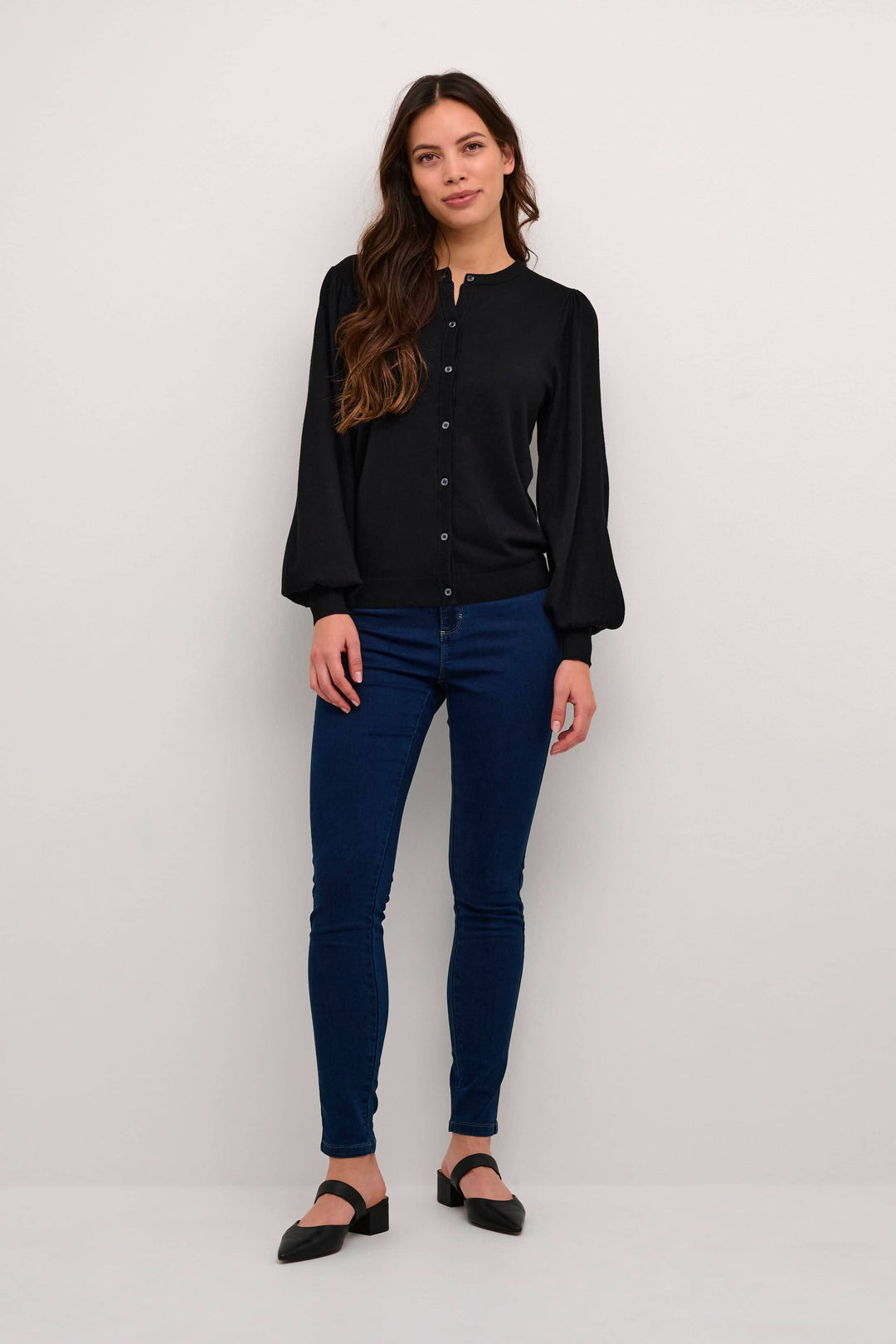 Femme portant un cardigan Lizza noir à manches ballons, associé à un jean bleu et des chaussures plates.