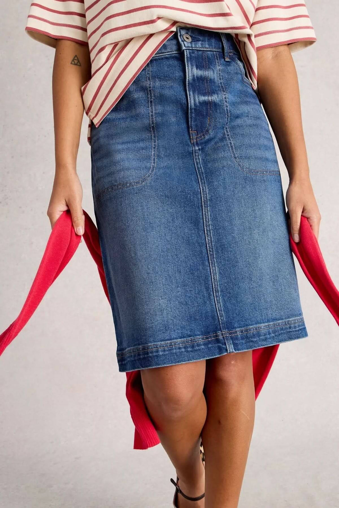 Jupe Tia en denim classique, coupe droite, taille haute, associée à un style casual chic avec T-shirt et baskets.