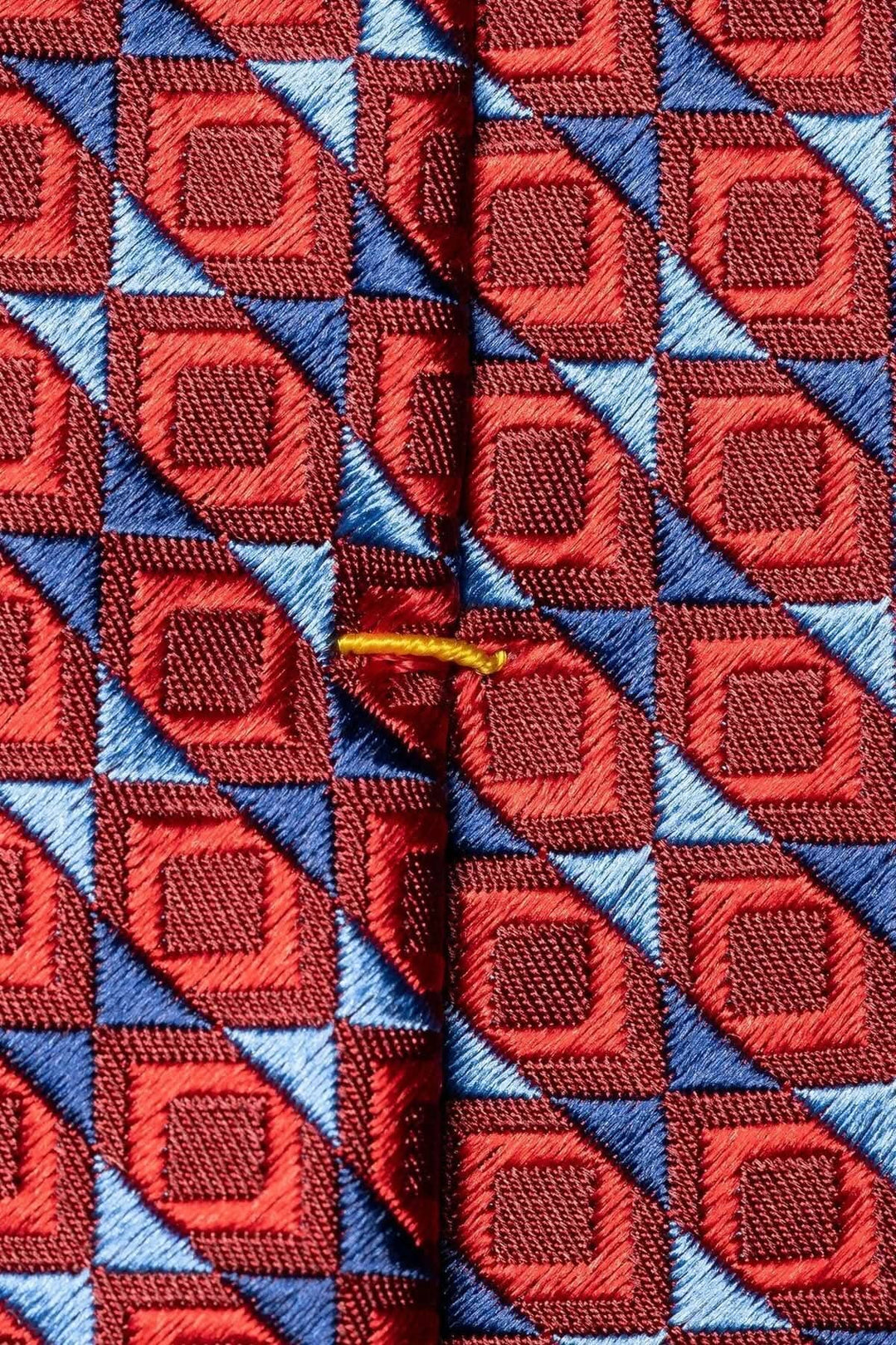 Cravate en soie avec motif géométrique rouge et bleu, ajoutant élégance à une tenue formelle.